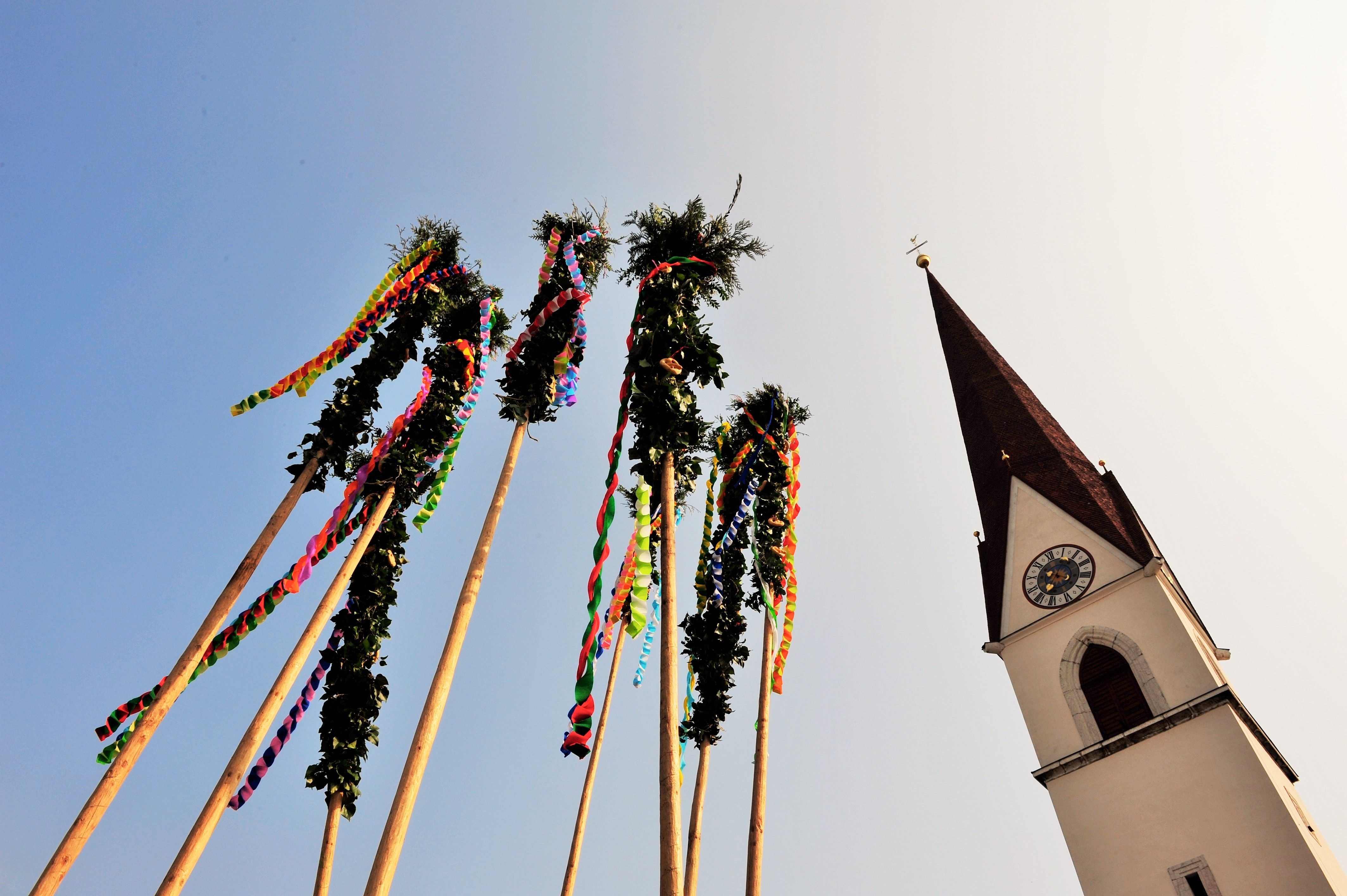 Mit Palmbuschen geschmückte Latten ragen neben der Kirche in Kramsach in den Himmel